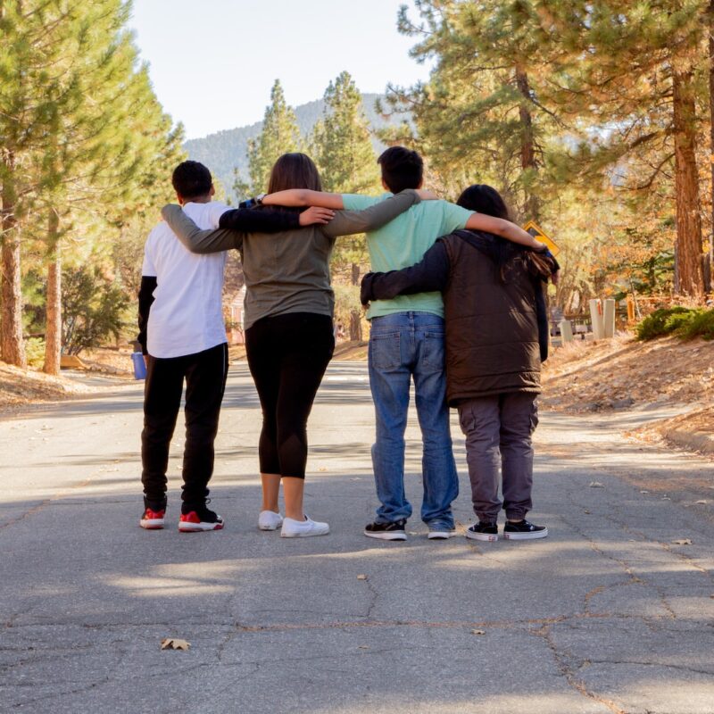 four people with hands on shoulders standing on road during daytime